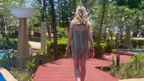Girl-walks-over-swimming-pool-bridge-at-tropical-resort-hotel