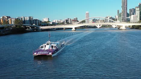 Drone-shot-tracking-City-Cat-Boat-on-Brisbane-River,-looking-towards-Brisbane-City-and-Bridges