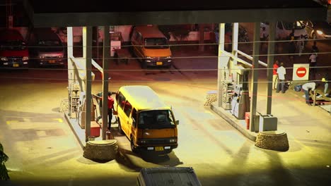 Areal-view-of-a-gas-station-at-night-with-attendants-fueling-a-commercial-bus-in-Africa,-Ghana