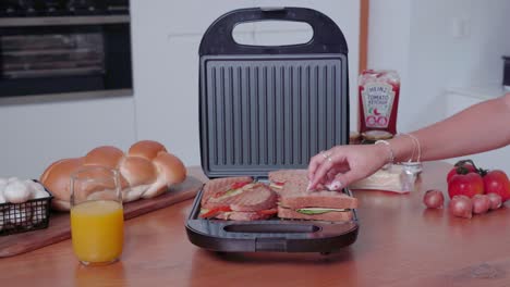Woman-putting-sliced-panini-sandwich-on-electric-grill-and-closing-lid-to-cook