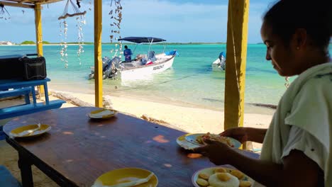 Latin-woman-serves-Venezuelan-arepas-food-typical-product,-beach-restaurant,-Los-Roques
