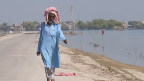 Older-Male-Pakistani-Male-Walking-Alone-Along-Path-Beside-Flooded-Land-In-Sindh