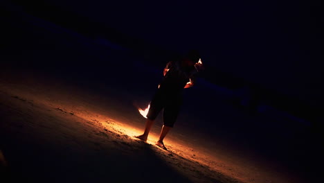 Skillful-performer-spinning-flaming-staff-at-night-fire-show-on-beach