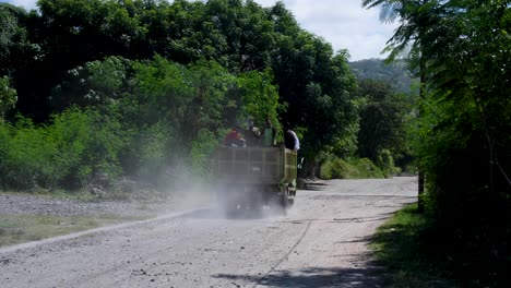 People-traveling-on-bumpy,-dusty-gravel-road-in-a-green-work-truck-on-remote-tropical-Atauro-Island-in-Timor-Leste
