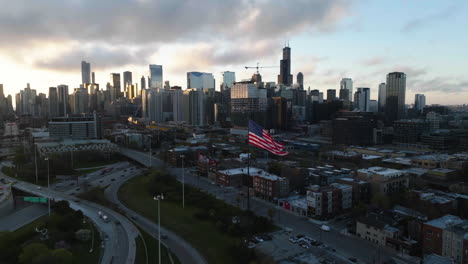 Static-drone-shot-of-a-US-Flag,-Interchange-90-and-the-Fulton-River-district,-sunrise-in-Chicago