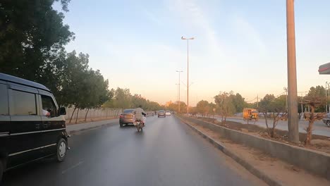 Karachi,-Pakistan:-Car-ride-on-a-busy-evening-in-Karachi-city,-Pakistan-with-cars-passing-by-and-historic-monument-visible-in-distance