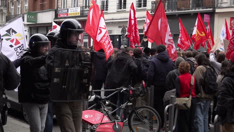A-unit-of-plain-clothes-riot-police-officers-carrying-shields-and-wearing-helmets-shadow-a-group-of-protestors-during-the-national-strike-action-and-protests-over-a-rise-in-the-pension-age