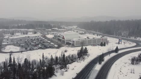 Luftaufnahme-Bei-Schneefall-In-Richtung-Ihres-Unabhängigen-Lebensmittelhändlers-In-Huntsville,-Kanada,-Winter