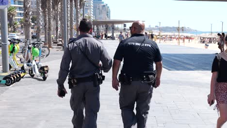 Dos-Policías-Armados-Caminando-Por-El-Paseo-Marítimo,-Vista-Posterior
