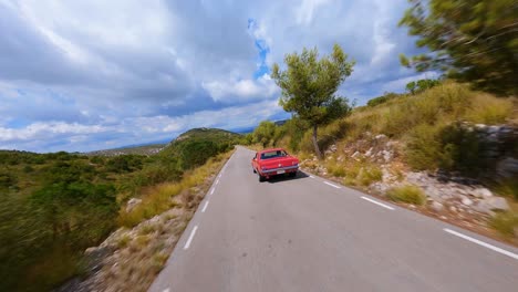 Gorgeous-and-cinematic-aerial-view-of-a-classic-red-Mustang-driving-through-a-scenic-mountain-landscape