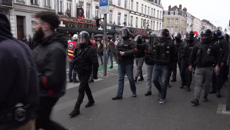 A-unit-of-plain-clothes-riot-police-officers-carrying-shields-and-wearing-helmets-walk-alongside-a-group-of-protestors-during-the-national-strike-action-and-protests-over-a-rise-in-the-pension-age