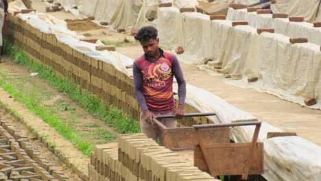 Arbeiter,-Die-In-Einer-Ziegelfabrik-In-Bangladesch-Mit-Ziegeln-Und-Schubkarren-Umgehen