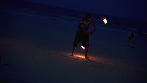 Performer-spinning-two-flaming-torches-at-night-at-beach-fire-show
