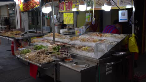 Lady-vendors-sell-lok-lok,-a-dish-consisting-of-various-steamboat-style-foods-of-meats-and-vegetables-served-on-a-skewer-at-Jalan-Alor,-Kuala-Lumpur,-Malaysia