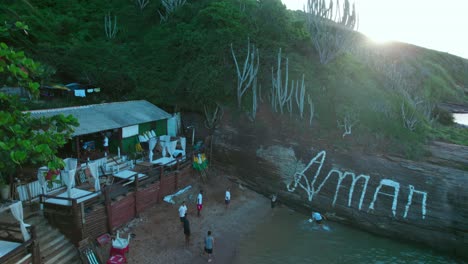 Junge-Brasilianische-Kinder-Spielen-Fußball-Am-Ufer-Des-Strandes-Von-Joao-Fernandes,-Um-Graffiti-Zu-Lieben,-Die-Auf-Einen-Steinhang-An-Der-Küste-Gemalt-Wurden