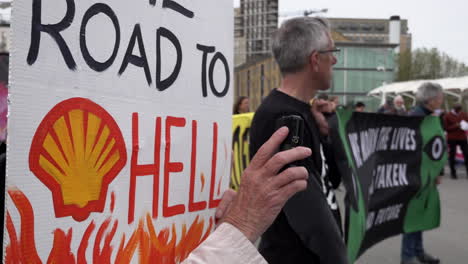 A-Climate-Change-activist-holds-a-placard-that-reads-“Road-To-Hell”-next-to-other-protestors-holding-a-banner-outside-the-Shell-Annual-General-Meeting-at-the-Excel-Exhibition-Centre