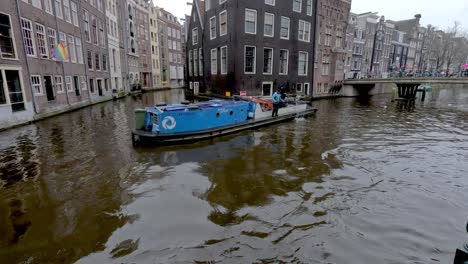 Municipal-council-worker-standing-on-a-barge-cleaning-rubbish,-trash-and-litter-from-a-canal-in-Amsterdam,-Netherlands