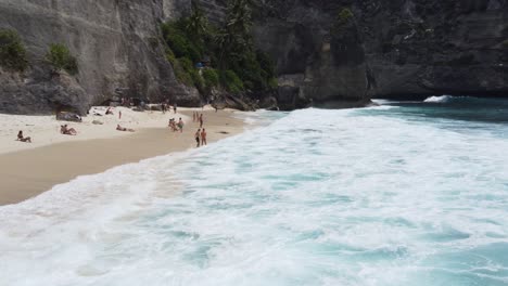 Tourists-swim-at-dramatic-Diamond-beach-with-epic-sea-cliffs,-Nusa-Penida