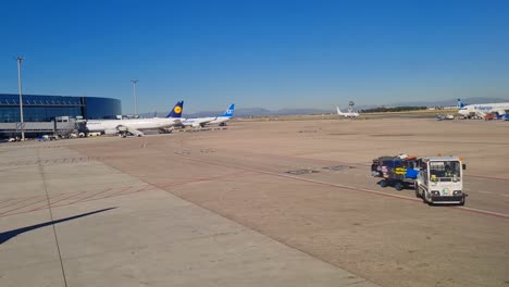 Small-Lorry-loaded-with-luggage-drives-on-the-airport-tarmac-surrounded-by-planes-in-Madrid,-Spain