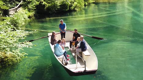 Cámara-Lenta-De-Familias-De-Turistas-Multiétnicos-Disfrutando-De-Un-Paseo-En-Bote-De-Primavera-Con-Fondo-De-Cristal-En-Aguas-Cristalinas-De-Color-Turquesa-Del-Famoso-Lago-Alpino-Blausee-En-Kandersteg,-Suiza