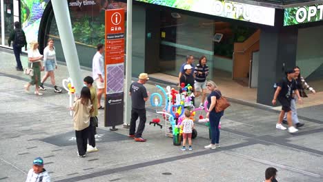Zeitrafferaufnahme-Der-Geschäftigen-Innenstadt-Von-Brisbane,-Talentierter-Straßenmusiker,-Der-Auf-Der-Straße-Im-Queen-Street-Mall,-Queensland,-Australien,-Kunstvolle-Ballon-Twister-Mit-Besonderer-Modellform-Verkauft