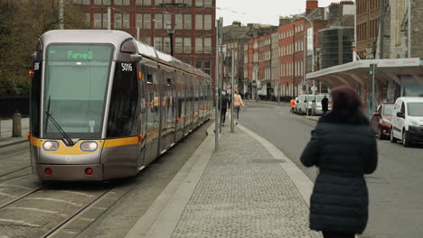 Woman-walking-away-from-camera-as-public-train-approaches-in-Dublin-Ireland
