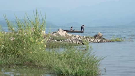 Dos-Pescadores-Sacando-La-Red-Del-Océano-En-Un-Pequeño-Bote-Remando-Hacia-La-Izquierda,-Tiro-Panorámico-Hacia-La-Izquierda