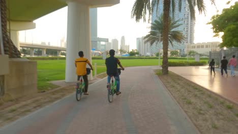 Witness-the-joy-of-two-cyclists-near-Dubai-Frame,-surrounded-by-lush-green-grass-along-the-highway