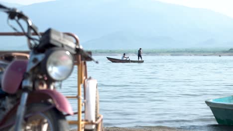 Two-Mexican-fishermen-pulling-nets-out-of-the-ocean-on-a-paddle-boat-with-motorcycle-close-to-view,-Pan-left-shot