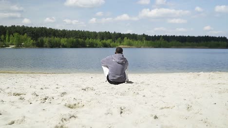 Young-man-sitting-alone-on-an-empty-lake-beach