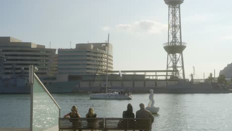 Großes-Segelboot-Sticht-Aus-Dem-Handelshafen-Von-Barcelona-In-See,-Menschen-Entspannen-Sich-Auf-Bänken-An-Der-Rambla-Del-Mar