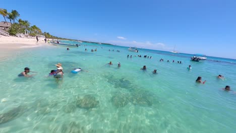 People-relaxing-and-swimming-in-tuquoise-ocean-water-of-Catalina-tropical-island-beach-in-Dominican-Republic-in-summer-season,-aerial-fpv-drone-view
