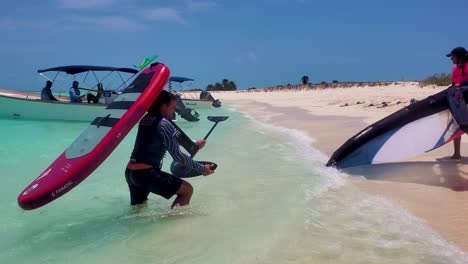 Couple-take-out-wing-foil-kite-from-sea-water-to-white-sand-beach-after-kitesurf-lesson