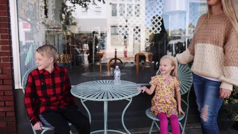 Boy-And-Girl-Sitting-At-Table-In-Small-Town-Smiling-Outdoors