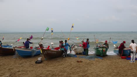 Weiter-Blick-Auf-Fischerboote-Am-Strand-Von-Thailand,-Die-Morgens-Ihren-Fang-Verkaufen-Und-Bei-Windigen-Bedingungen-Netze-Zurück-Auf-Das-Traditionelle-Holzboot-Laden