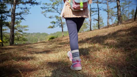 A-little-girl-with-a-tiny-backpack-and-feet-in-sneakers-walking-along-path-in-the-autumn-forest