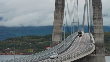 Cars-a-heavy-truck-carrying-a-bulldozer,-and-a-motorhome-pass-along-the-curves-of-the-Halogaand-Bridge-above-the-fjord