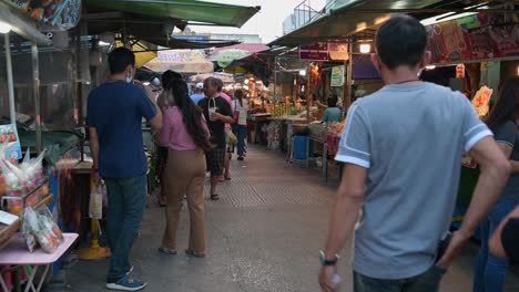 People-walking-down-the-street-as-they-prospect-for-food-and-somethings,-Amphawa,-Samut-Songkhram,-Thailand