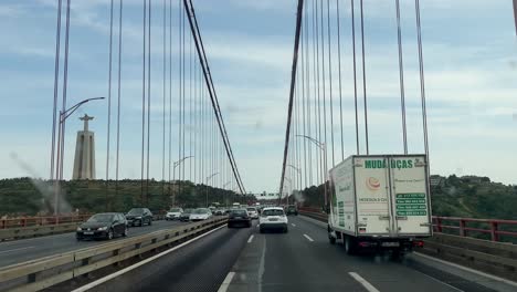 Pov-drive-on-famous-Ponte-25-de-Abril-Bridge-in-Lisbon-and-Christ-the-King-Statue-in-background