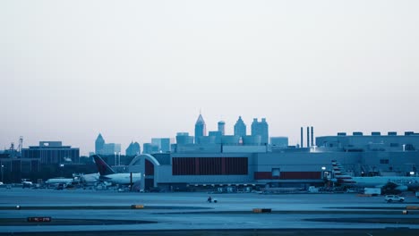 Eine-Teleaufnahme-Von-Delta-Verkehrsflugzeugtaxis-Am-Flughafen-Atlanta-Mit-Der-Skyline-Von-Atlanta,-Georgia-Im-Hintergrund-Am-Morgen