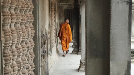 2-Buddhist-Monk-walking-and-through-the-interior-of-the-Ancient-Temple-of-Angkor-Wat---Siem-Reap,-Cambodia
