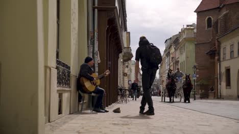 Street-Musician-Performing-Guitar-Song-in-Old-Town,-while-Young-Boy-Gives-him-Money