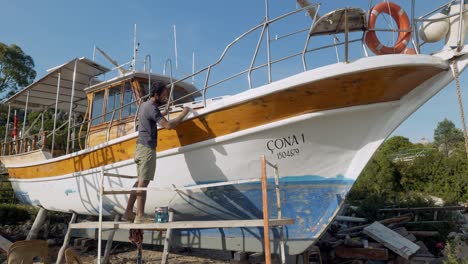 Man-paints-hull-of-boat-in-dry-dock-preparation-for-holiday-tourists-season
