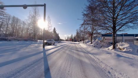Im-Winter-Navigiert-Das-Auto-Elegant-über-Die-Von-Bäumen,-Häusern-Und-Anderen-Fahrzeugen-Gesäumte-Straße,-Während-Die-Sonne-Die-Umgebung-Beleuchtet