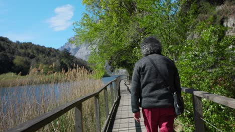POV-Behind-Person-Walking-Along-Boardwalk-On-Lake-Toblino-In-Italy