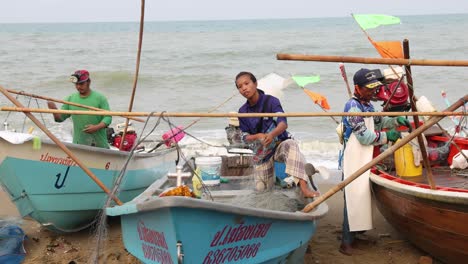 Wide-view-of-fishermen-loading-nets-on-wooden-fishing-boats-after-selling-catch-at-morning-market-on-beach