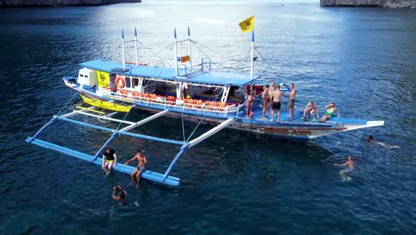 Group-of-young-tourists-People-enjoying-island-hopping-tour-swimming,-jumping-off-Outrigger-boat-El-Nido---Philippines