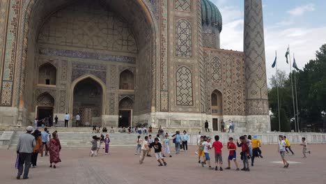 Kids-Playing-in-Front-of-Sher-Dor-Madrasah,-Monumental-Landmark-of-Samarkand,-Uzbekistan