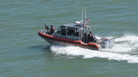 Close-up-shot-of-US-Coast-guard-high-speed-boat-cuts-through-the-ocean-waves,-with-a-valiant-soldier-standing-strong,-armed-with-a-machine-gun-|-US-Coast-guard-armed-force-on-duty