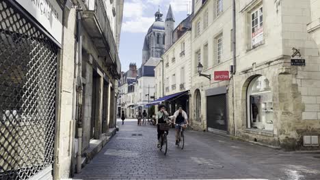 Walking-on-a-street-in-Tours-city,-France-with-the-view-towards-dome-of-the-Basilica-Saint-Martin-while-cyclists-are-passing-by